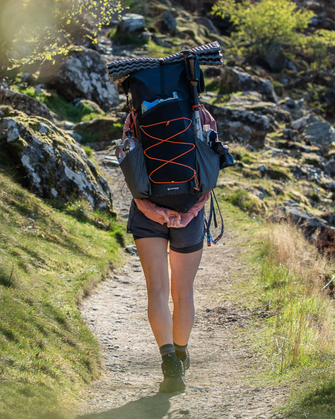 A hiker viewed from behind on a rocky dirt trail, wearing a fully loaded Prospector.